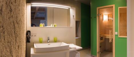 Un baño moderno con un espejo grande, lavamanos blanco y paredes verdes.