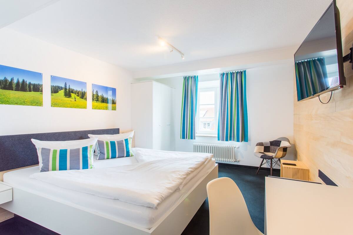 Een hotelkamer met een bed, een bureau, een stoel, een televisie en drie landschapsprenten aan de muur.