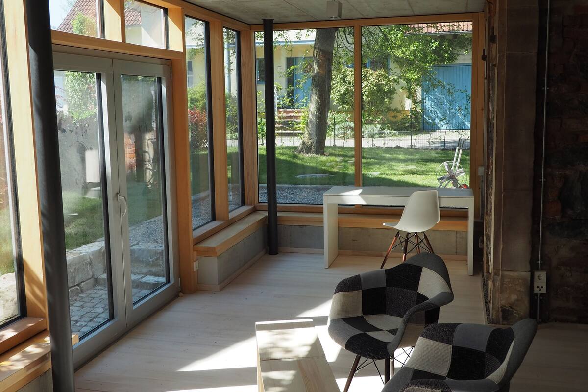Een ruime kamer met grote ramen, een houten bank en twee stoelen.