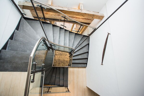 Una escalera moderna con barandillas de vidrio, vigas de madera y una combinación de pisos oscuros y claros.