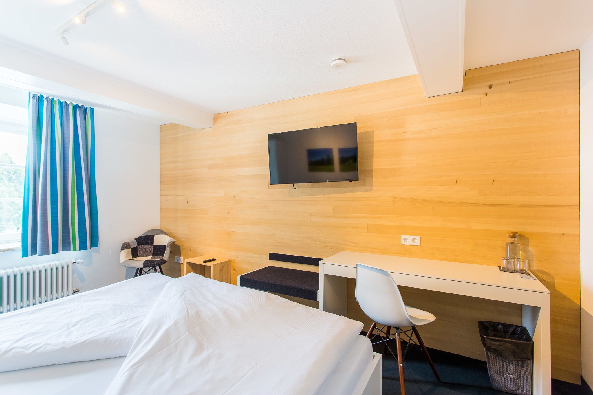 Ein Hotelzimmer mit Bett, Schreibtisch, Stuhl, an der Wand montiertem Fernseher und einem Fenster mit Vorhängen.