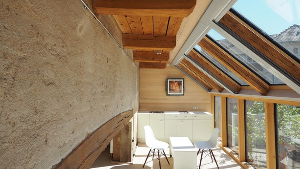 A modern interior with a sloped ceiling, wooden beams, a white desk, and chairs. - DIE KRONE - Hotel Garni (Kirchzarten)