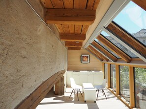 Un interior moderno con techo inclinado, vigas de madera, un escritorio blanco y sillas.