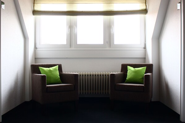 Una habitación con dos sillones y un radiador entre ventanas.