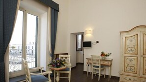 A room with a desk, two chairs, a small table with a vase of flowers, a TV on the wall, and a large cabinet with decorative panels. - La Rada B&B (Bacoli)