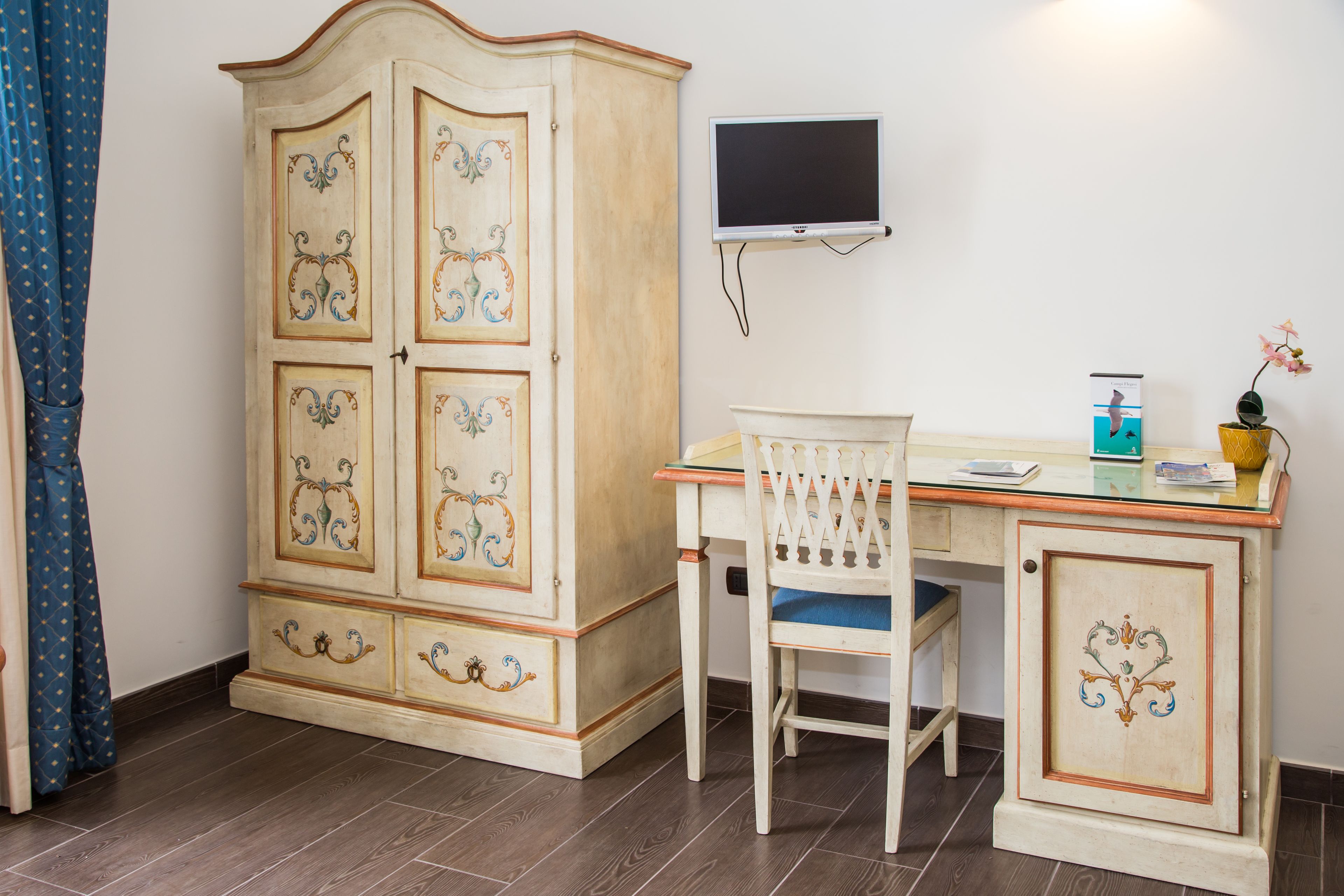 Une pièce comprenant un meuble en bois, un bureau avec une chaise, un téléviseur à écran plat et une petite plante en pot.