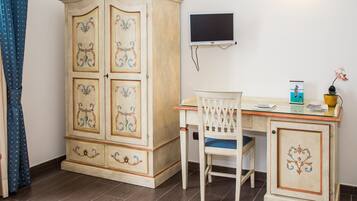 Une pièce comprenant un meuble en bois, un bureau avec une chaise, un téléviseur à écran plat et une petite plante en pot.