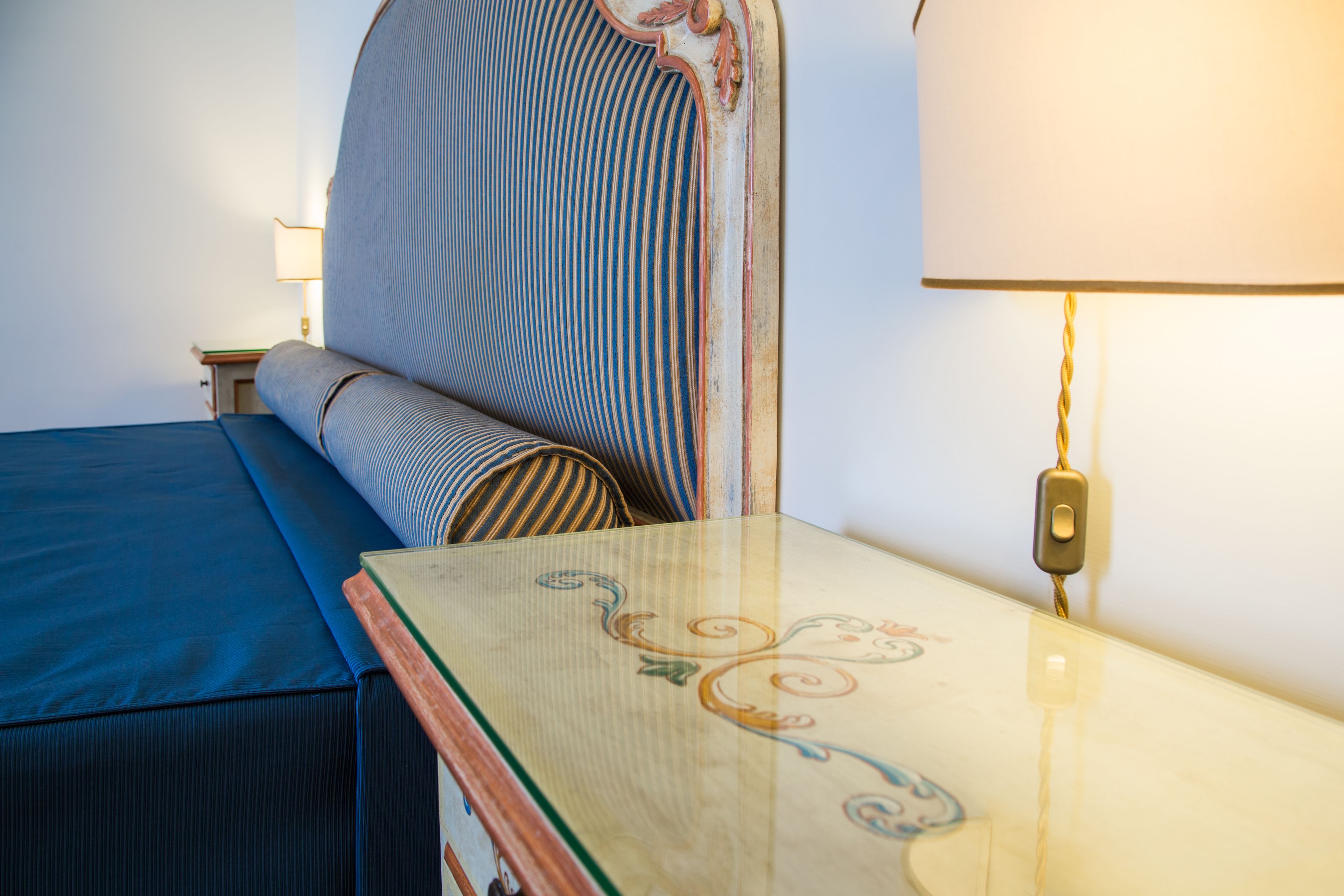 A neatly made bed with a striped headboard, a bedside table with a lamp, and a blue bedspread.