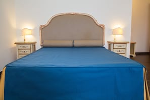 Una cama con cabecera a rayas, dos mesitas de noche con lámparas y una colcha azul.