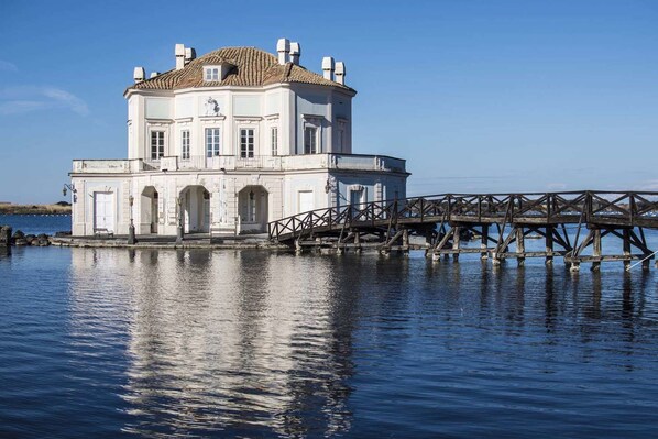 A white building with a tiled roof, a balcony, and a wooden pier extending into the water. - La Rada B&B (Bacoli)
