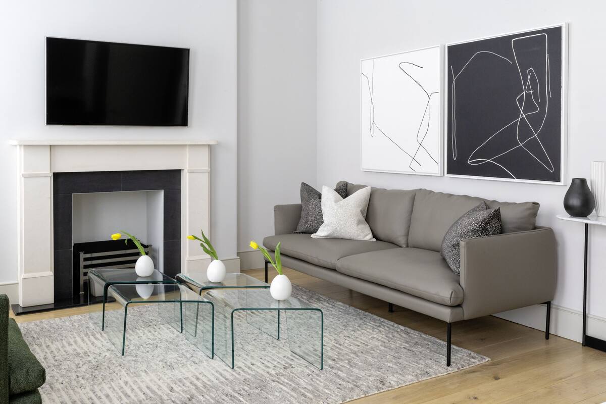 A modern living room with a grey sofa, a glass coffee table, a fireplace, and abstract wall art.