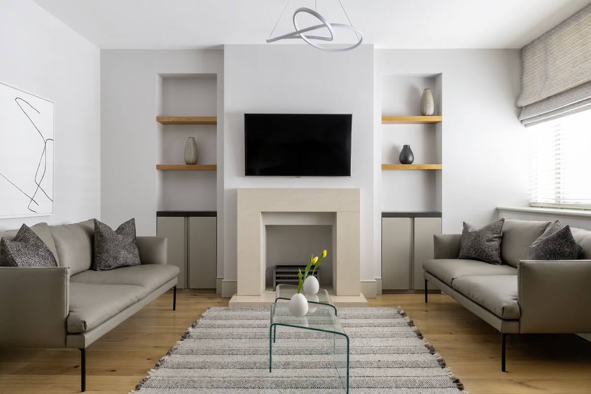 A modern living room with a flat-screen TV, two sofas, a fireplace, and a minimalist decor.