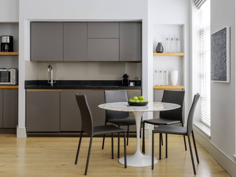 A modern kitchen with grey cabinets, a black countertop, and a round dining table with chairs.