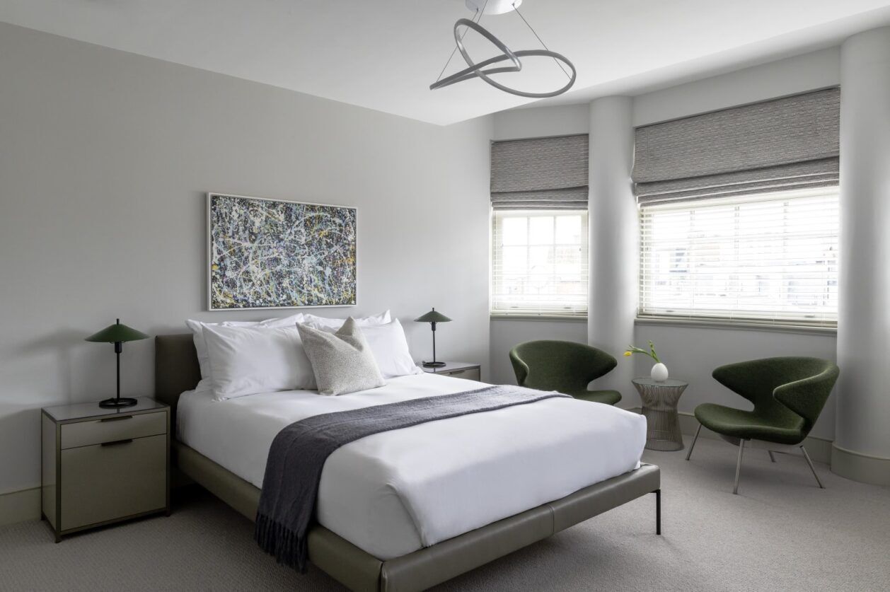 A modern bedroom with a large bed, two bedside tables, a green chair, and a floor lamp.