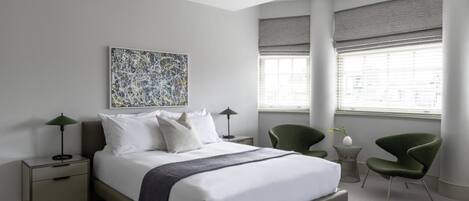A modern bedroom with a large bed, two bedside tables, a green chair, and a floor lamp.