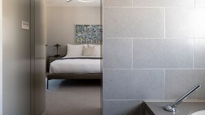 A modern hotel room with a bed, a nightstand, a lamp, and a bathroom with a shower. - AKA Marylebone (London)