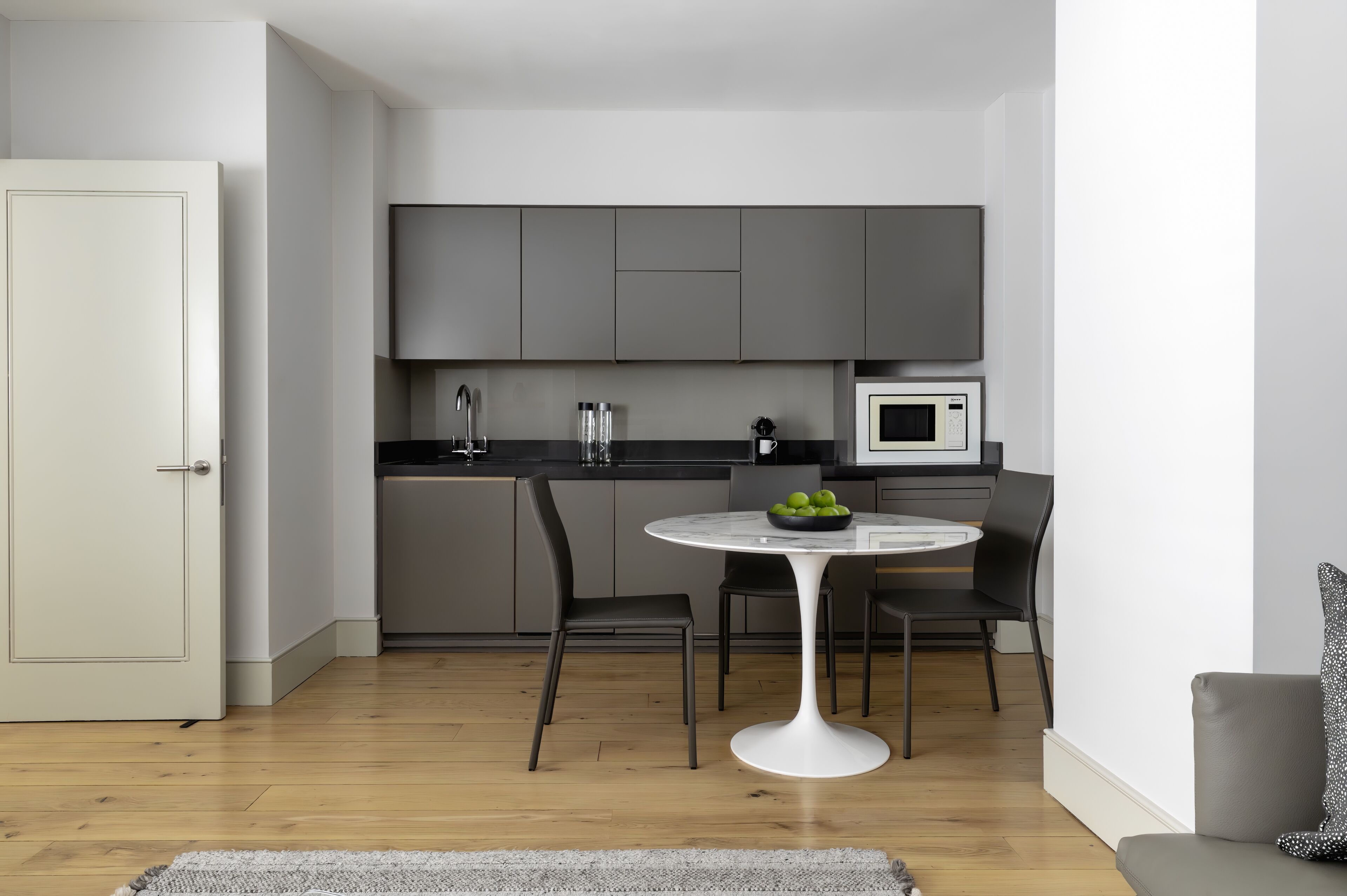 A modern kitchen with grey cabinets, a white microwave, and a round table with chairs.