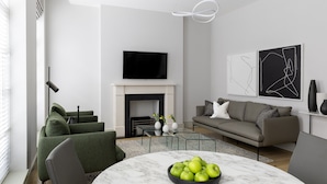 A modern living room with a fireplace, green sofas, a round marble table with a bowl of apples, and abstract wall art. - AKA Marylebone (London)