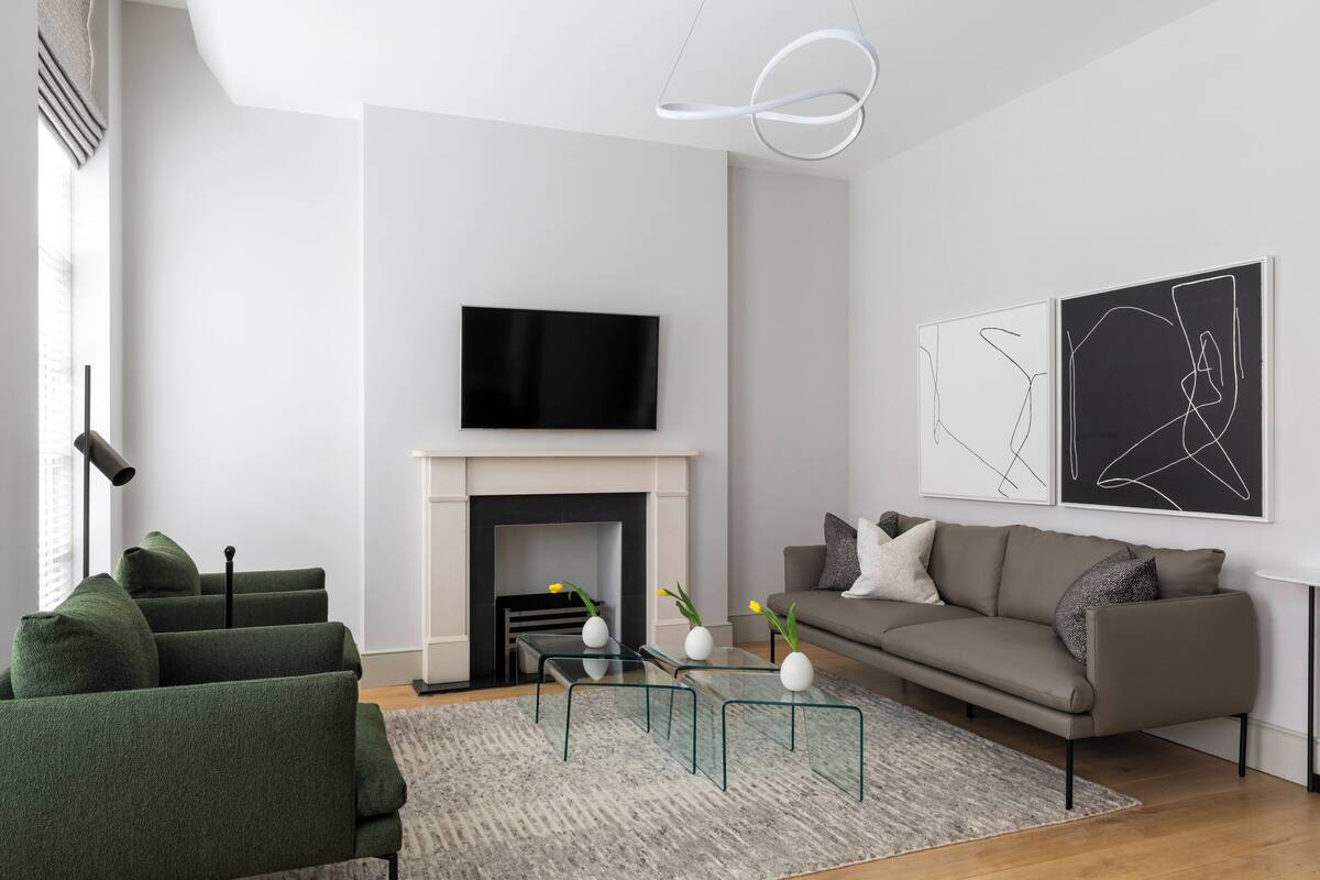 A modern living room with a fireplace, green sofas, a glass coffee table, and abstract wall art.