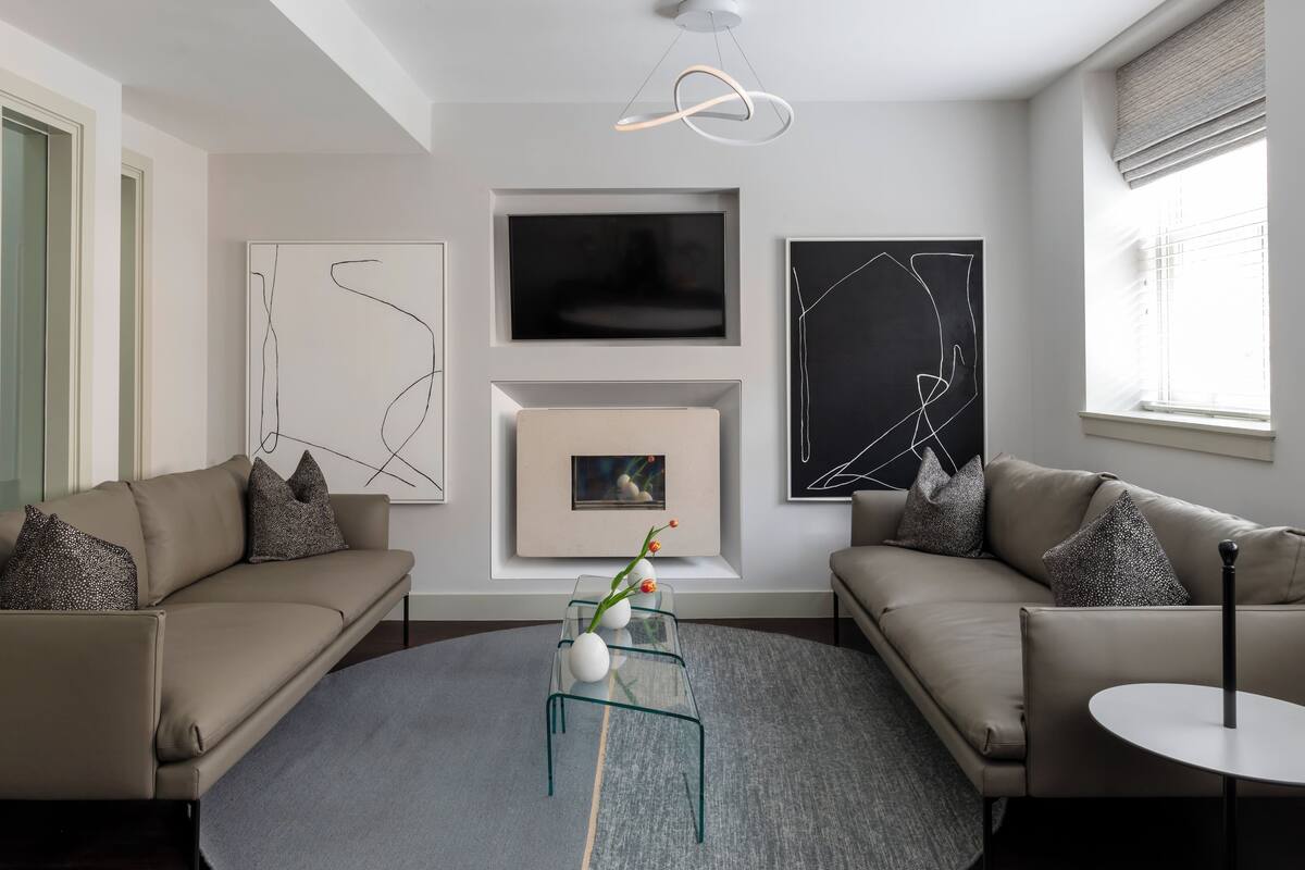 A modern living room with two sofas, a glass coffee table, abstract wall art, and a TV.