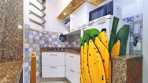 Una cocina con gabinetes blancos, un microondas y un refrigerador. El respuesto tiene un diseño de plátano.