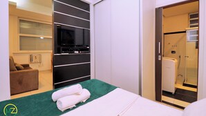 Habitación de hotel con cama, televisor, sofá y baño visible a través de una puerta abierta.