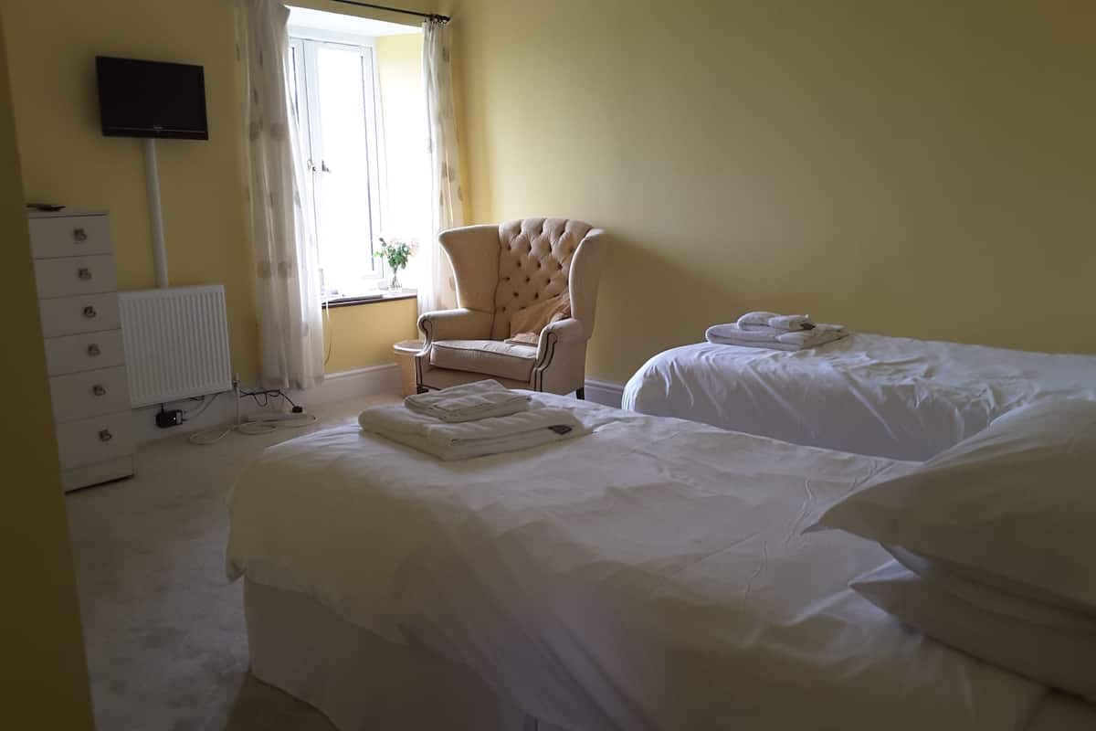 Une chambre d’hôtel avec deux lits, une chaise, une commode et un téléviseur fixé au mur.