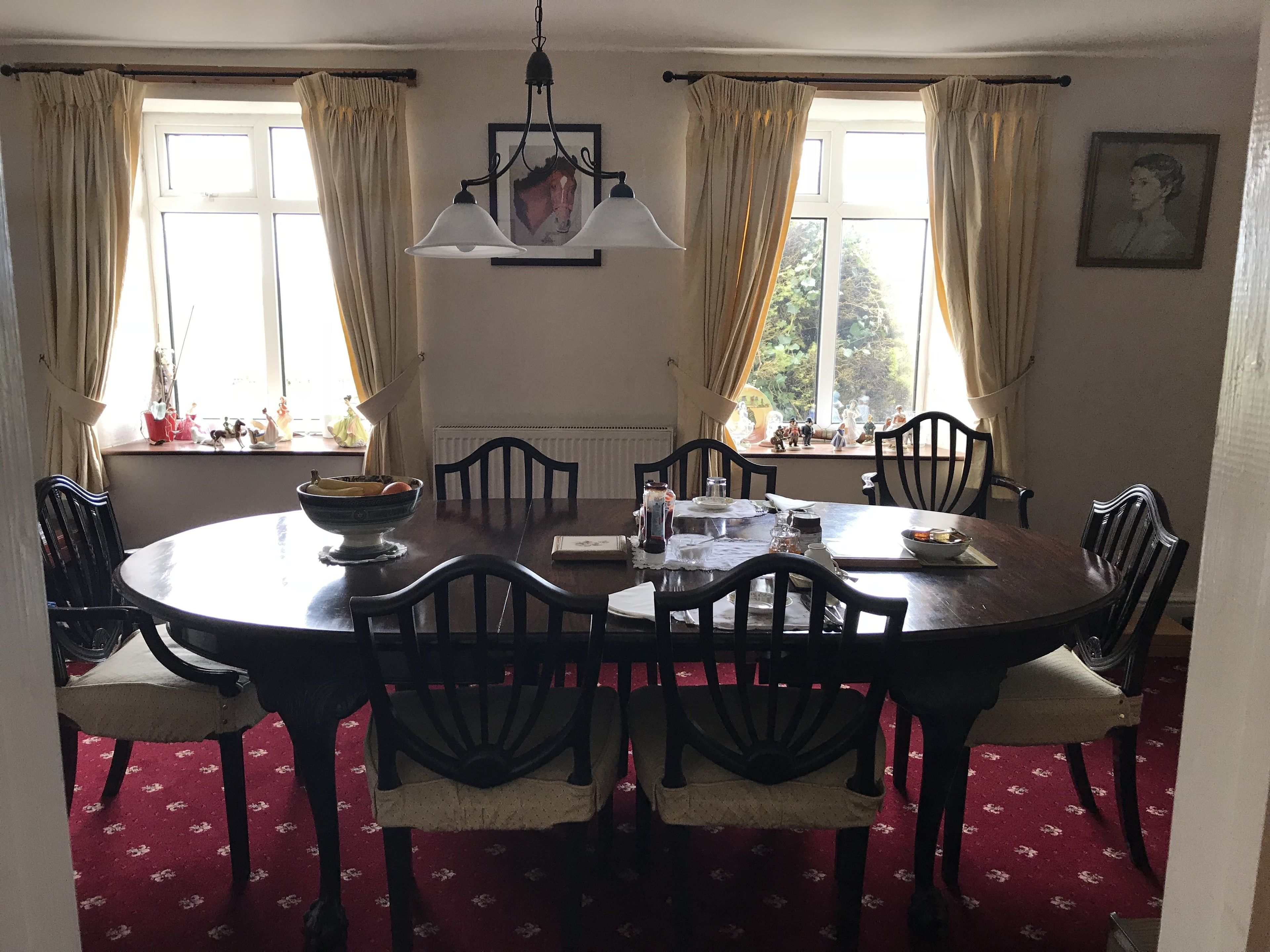 A dining room with a round table, chairs, a chandelier, and windows with curtains.