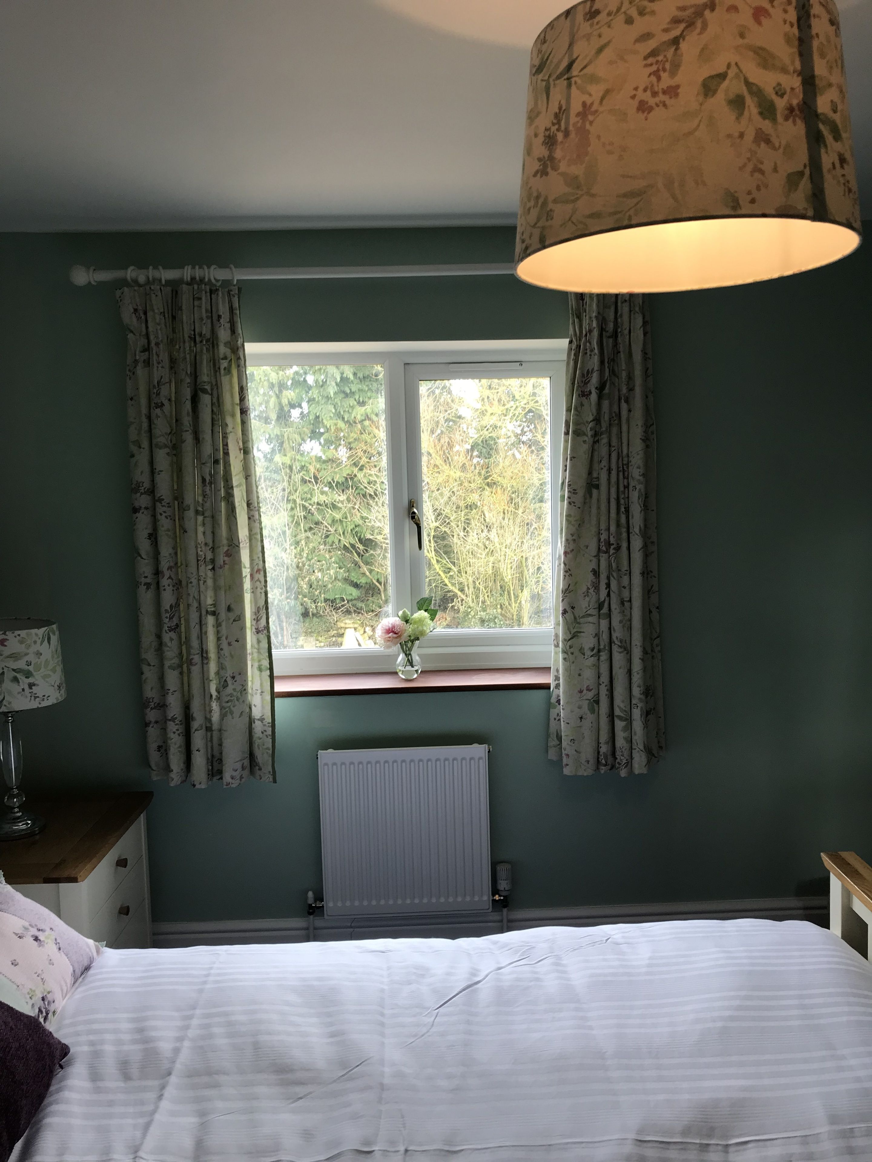 A bedroom with a bed, a window with curtains, a radiator, and a hanging lamp.