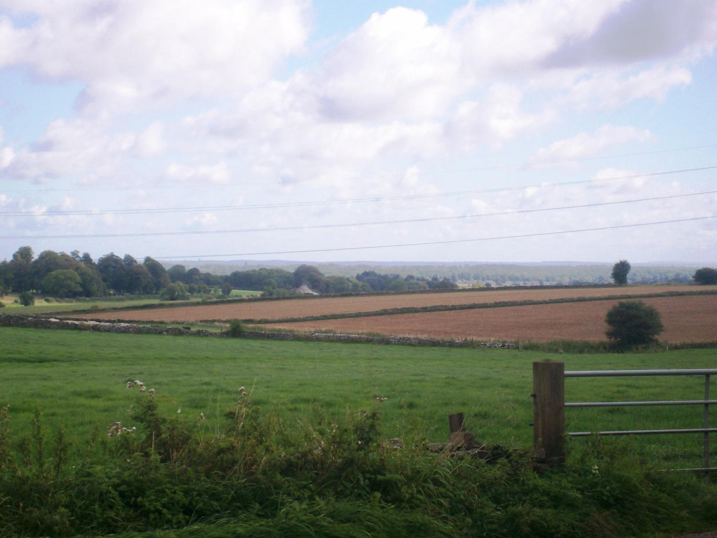A rural landscape with fields, a stone wall, and a wooden fence.