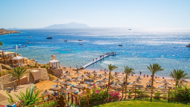 A beach resort with a pier, sun loungers, umbrellas, and a view of the sea.