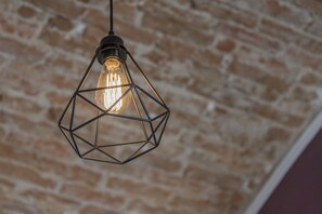A hanging light fixture with a geometric design against a brick wall. - Villa Santadi Hotel (Santadi)