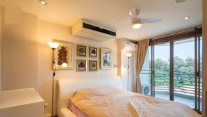 A hotel room with a bed, a standing lamp, air conditioning, and a view of greenery through the window. - Rayong by Milanee (Rayong)
