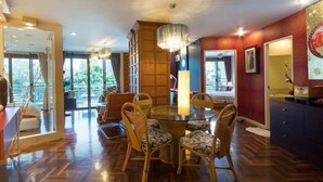 A dining area with a round glass table and wicker chairs, a chandelier, and a view through large windows. - Rayong by Milanee (Rayong)