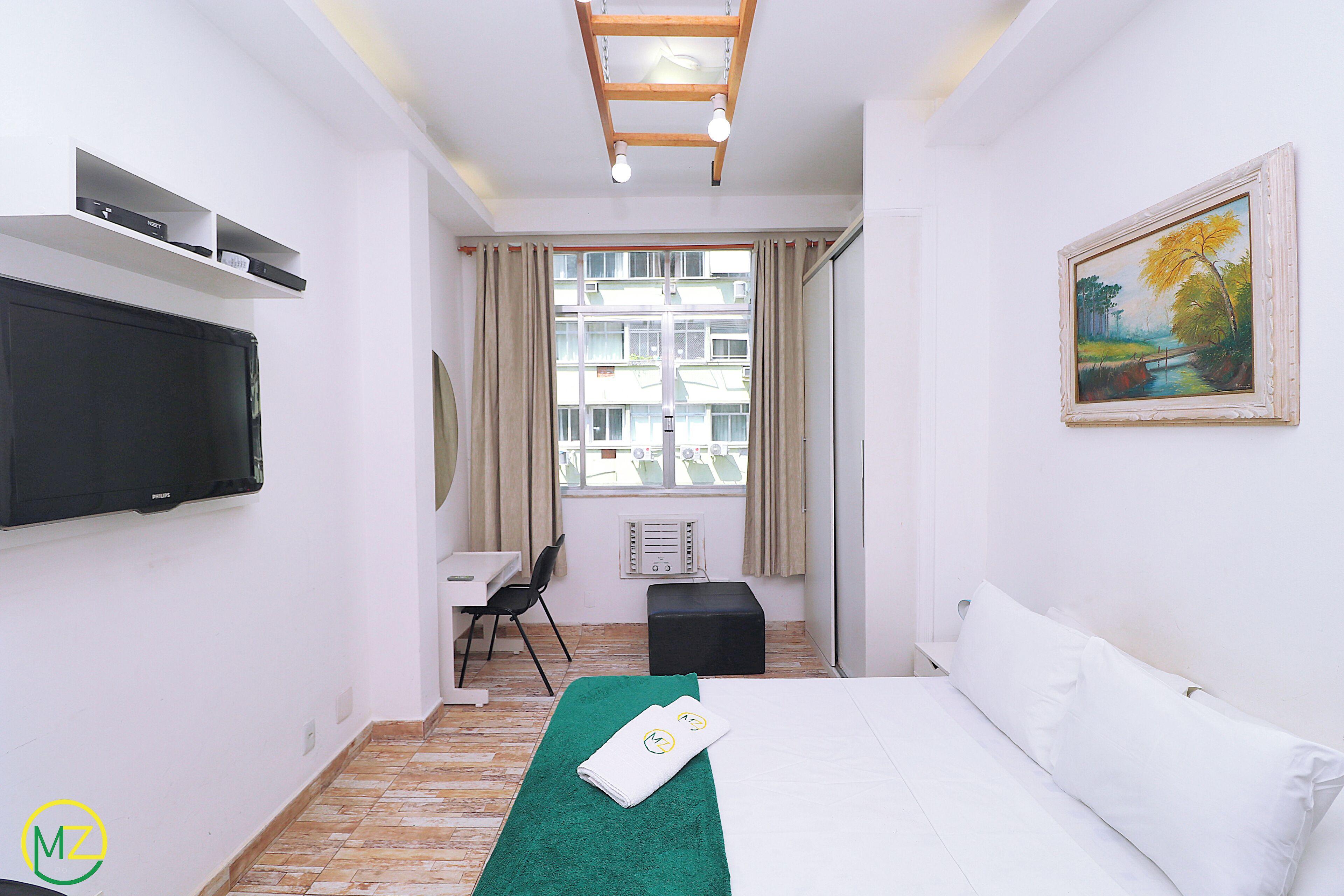 Una habitación de hotel con cama, escritorio, silla, televisión y ventana con cortinas.