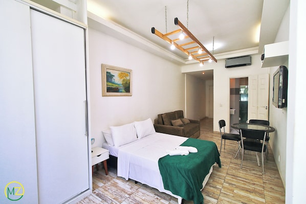 Une chambre d’hôtel avec un lit, une couverture verte, une chaise, une table et un tableau au mur.