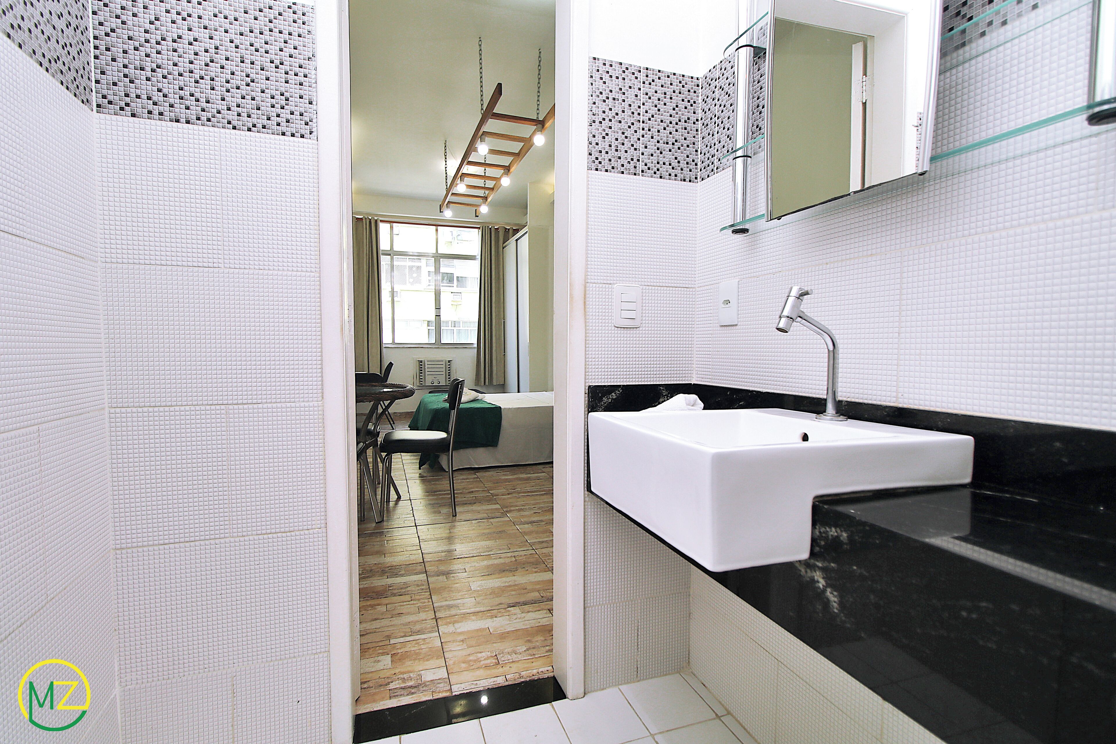 A modern bathroom with a white sink, black countertop, and a shower area with a wooden ladder.