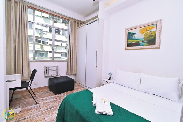 A hotel room with a bed, a desk, a chair, a radiator, and a painting on the wall. - MZapartments Prado LB613 (Rio de Janeiro)