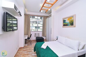 A hotel room with a bed, a desk, a chair, a TV, a painting, and a window with curtains. - MZapartments Prado LB613 (Rio de Janeiro)