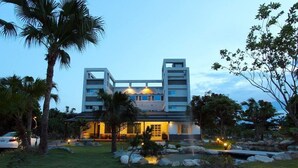 A modern hotel with a symmetrical facade, multiple balconies, and a well-maintained garden with palm trees and a small pond. - The Green Mile Field B&B (Ji'an)