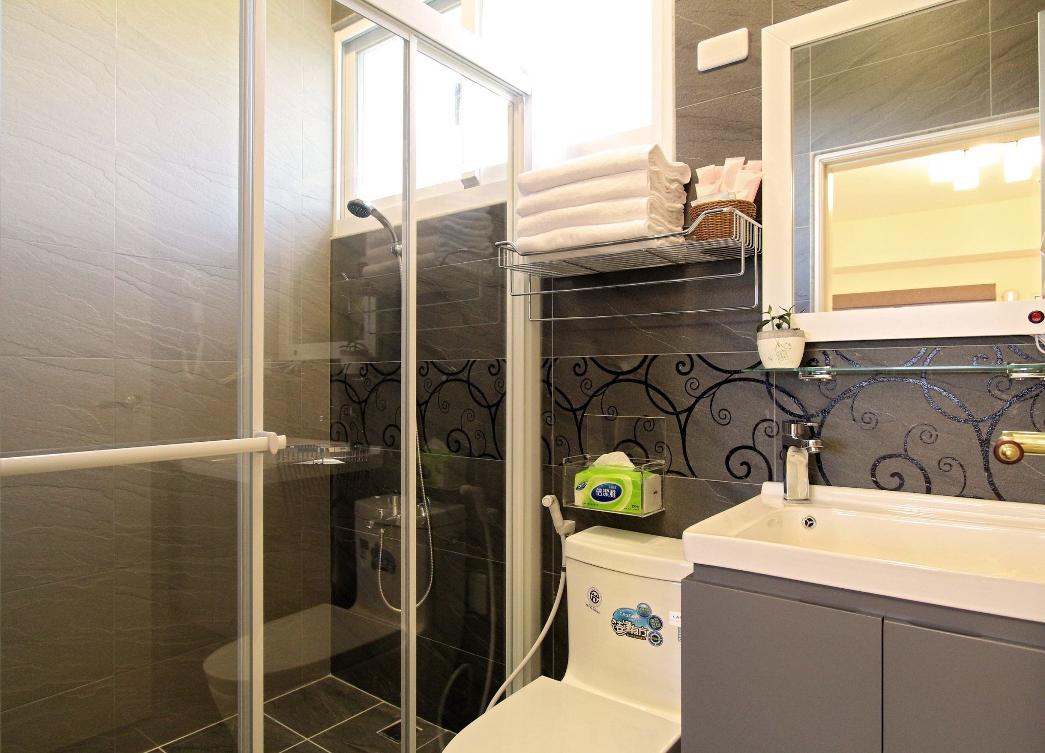 Ein Badezimmer mit Duschkabine aus Glas, Toilette und Waschbecken mit Spiegel darüber.