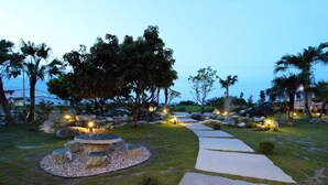 A landscaped garden with a stone fire pit, walking paths, and palm trees. - The Green Mile Field B&B (Ji'an)