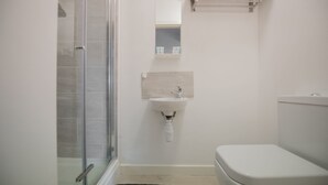 A bathroom with a glass shower enclosure, a white sink, and a toilet. - Kirkstall Bridge Apartments - 23 (Leeds)