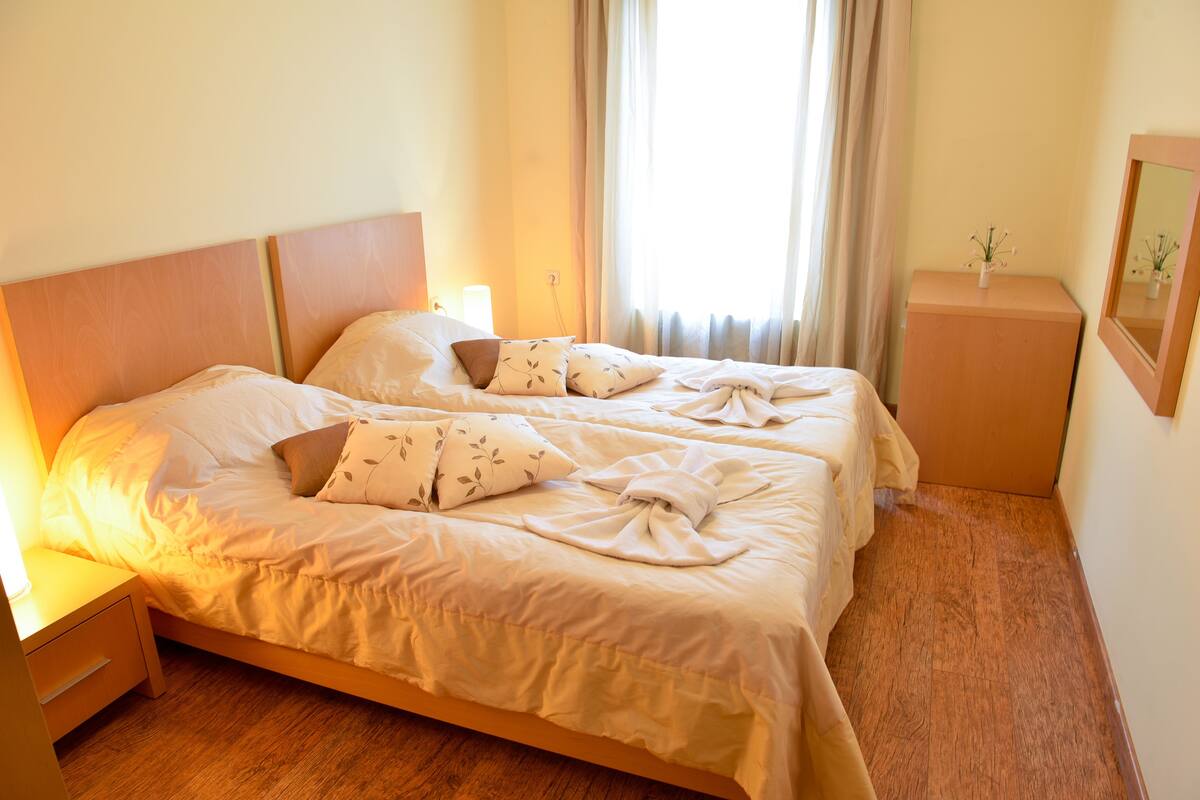 Ein Doppelbett mit hölzernem Kopfteil, ein Nachttisch und eine kleine Holzkommode mit Spiegel.