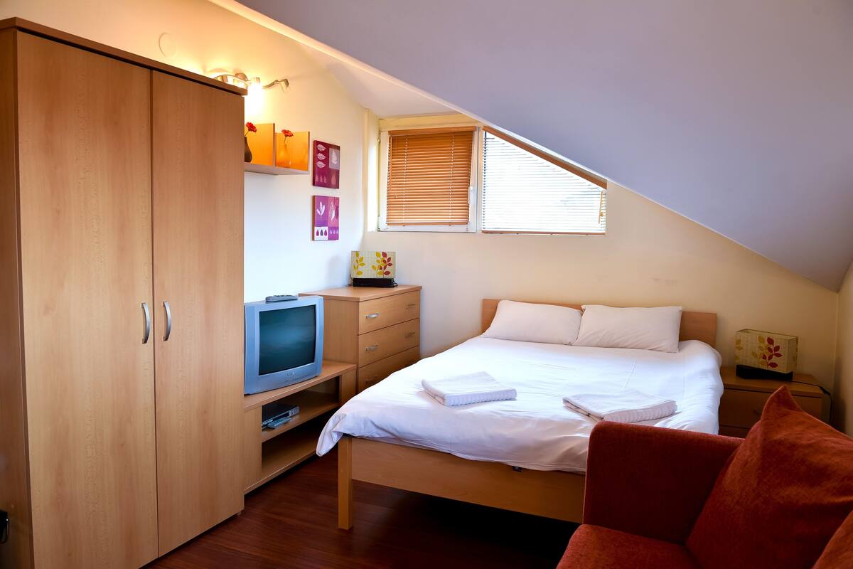 Ein Schlafzimmer mit Bett, Fernseher, Kleiderschrank und einem Fenster mit Jalousien.