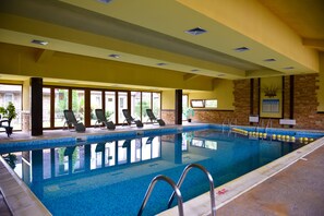 An indoor swimming pool with clear blue water, sun loungers, and a view of the outside. - Bojur & Bojurland Apartment Complex (Bansko)