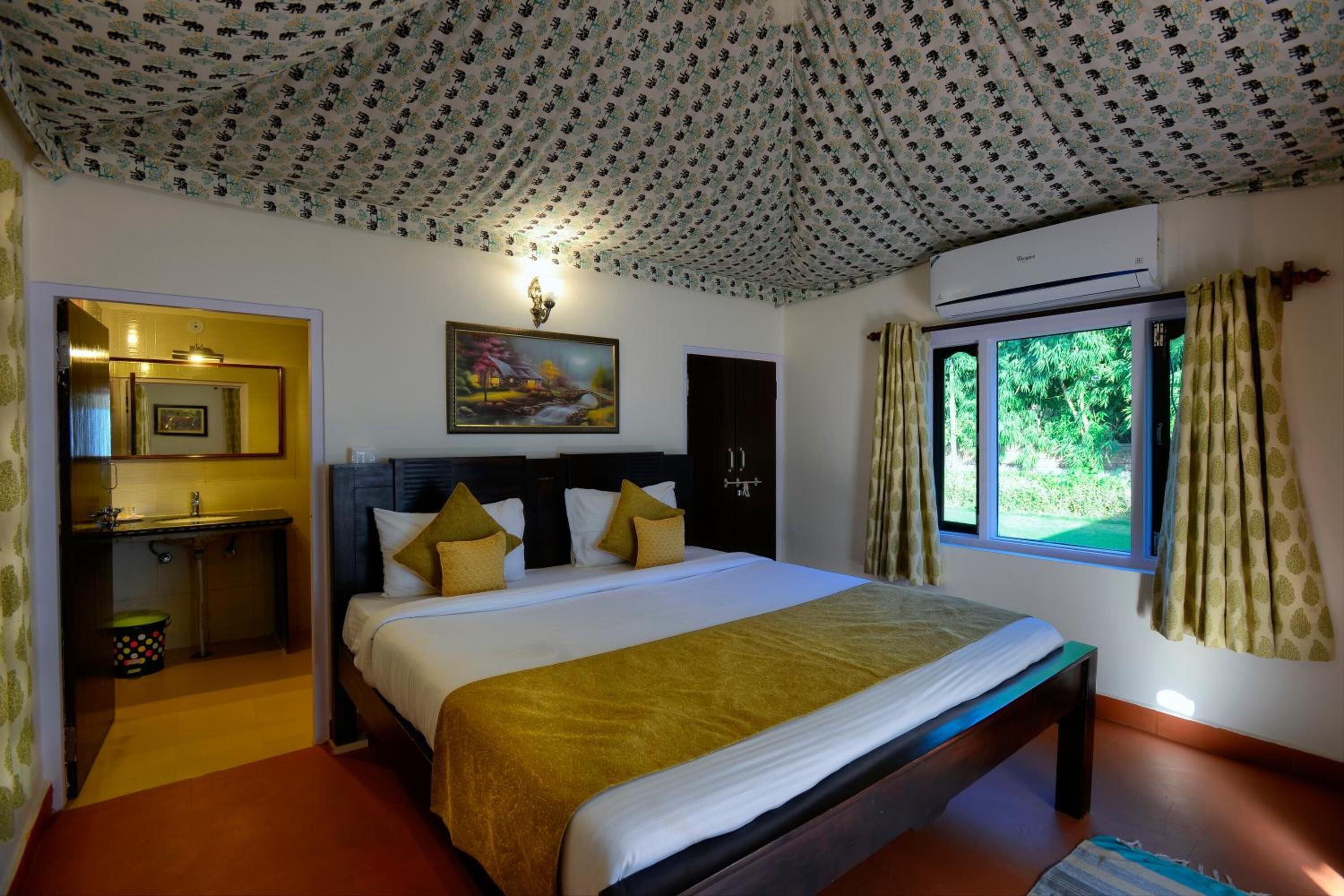 Un dormitorio con cama, mesita de noche, espejo, cuadro, aire acondicionado y ventana con cortinas.