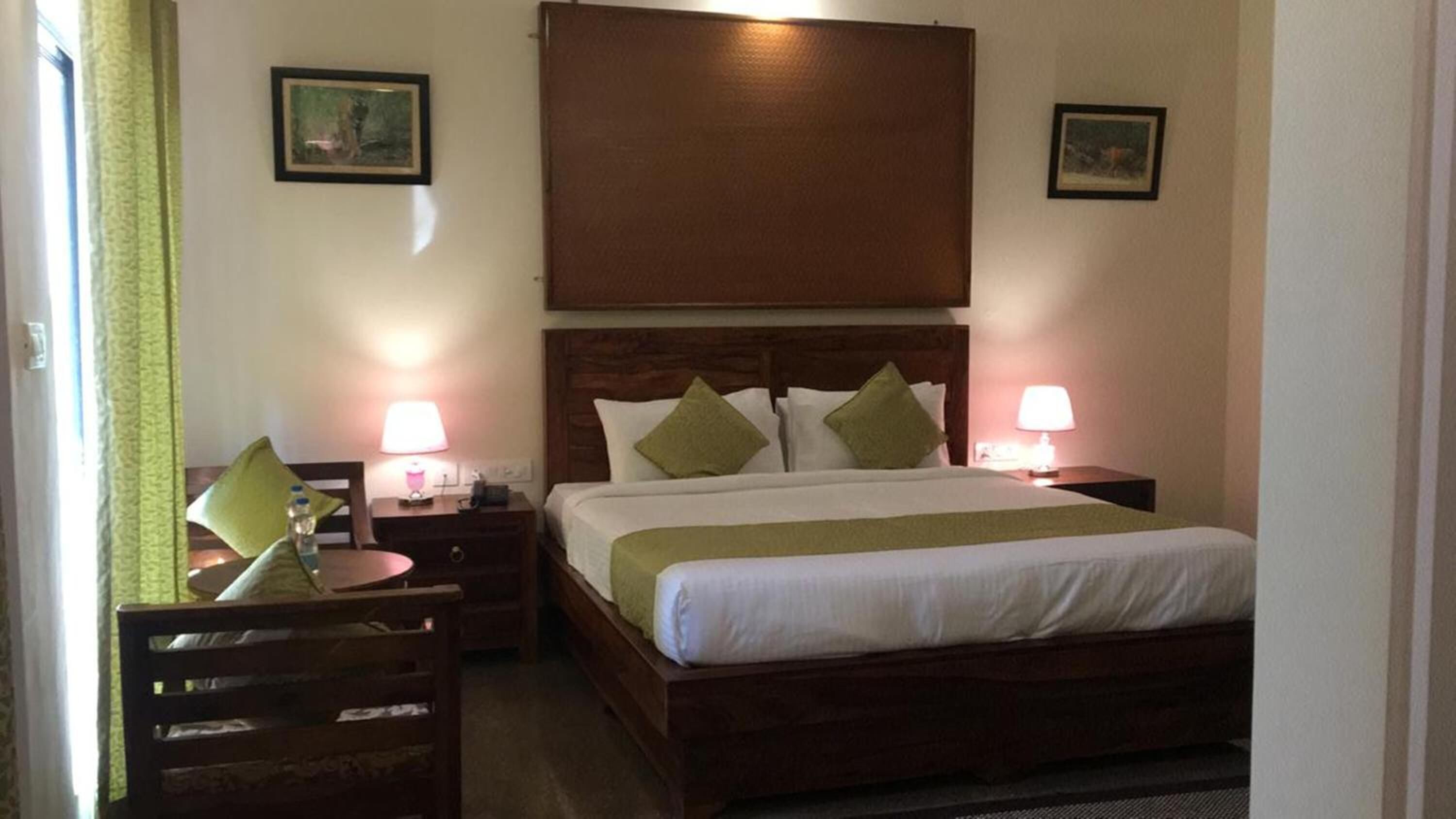 Una habitación de hotel con una cama, dos mesitas de noche con lámparas, una silla y dos cuadros en las paredes.