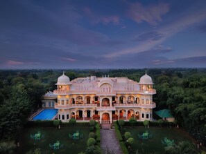 A large, ornate building with multiple domes and arches, surrounded by lush greenery and a swimming pool. - Ranthambhore Heritage Haveli (Sawai Madhopur)