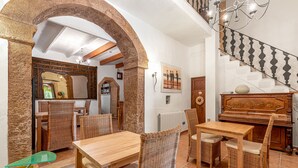Un coin repas avec des meubles en osier, un piano en bois et un escalier orné d’une rampe à motifs.